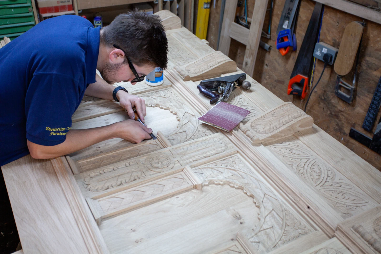 Craftsperson hand carving decorative detail into an overmantel component in the workshop
