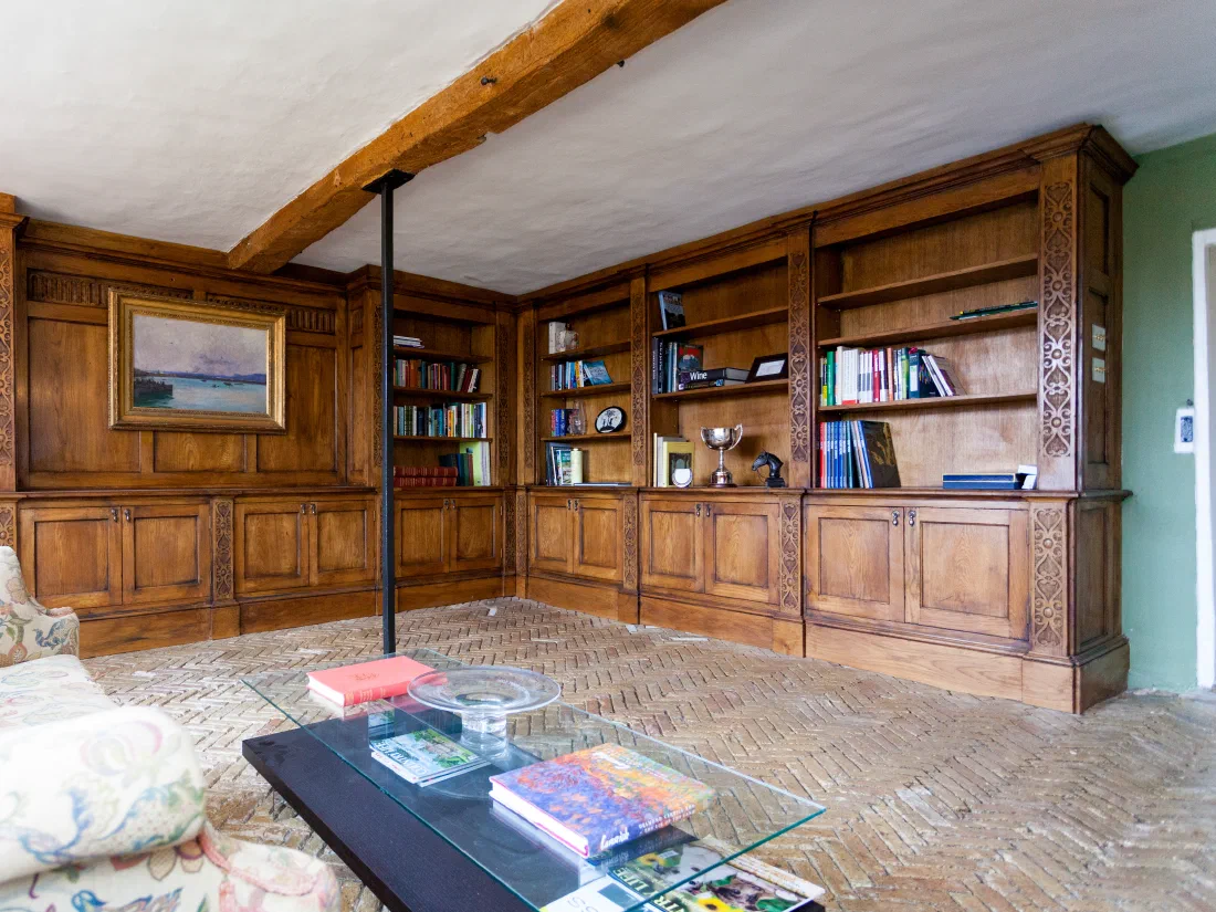 Fitted oak bookcases and cupboards beneath exposed ceiling beams