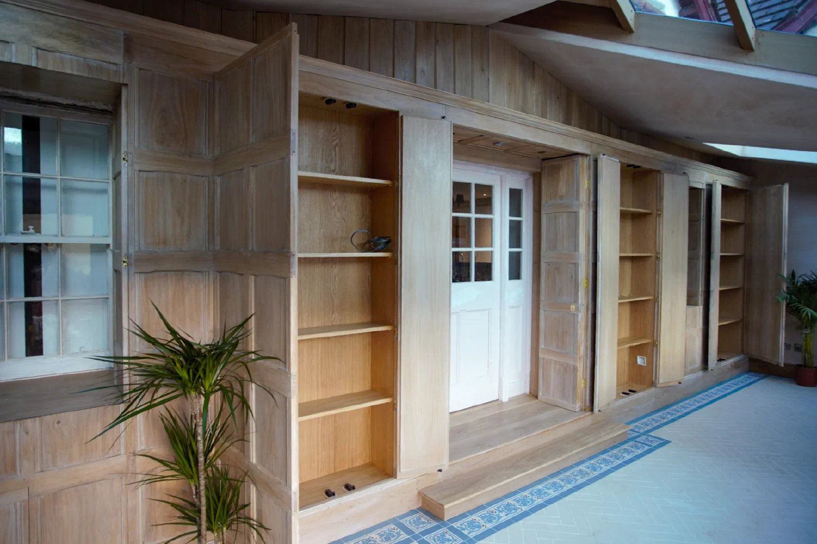 Unfinished oak panelling with integrated shelving and panelled doors fitted within a room