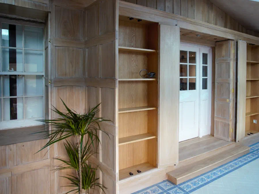 Unfinished oak panelling with integrated shelving and panelled doors fitted within a room