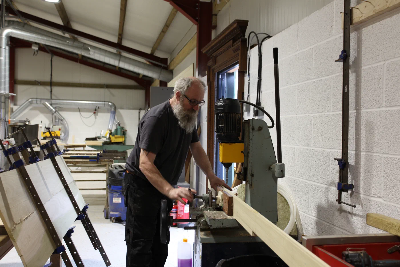 A craftsperson cutting mortices in a long timber component on a mortising machine in the Somerset workshop