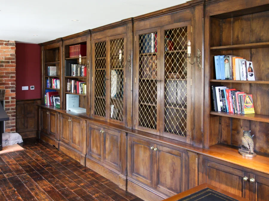 Fitted timber bookcases with open shelves, solid-brass open-mesh grilles and lower cupboards beside a brick fireplace