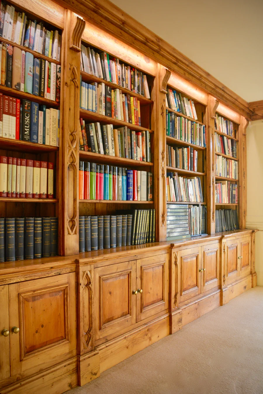 Tall fitted bookcases with carved uprights, integrated lighting and panelled cupboards
