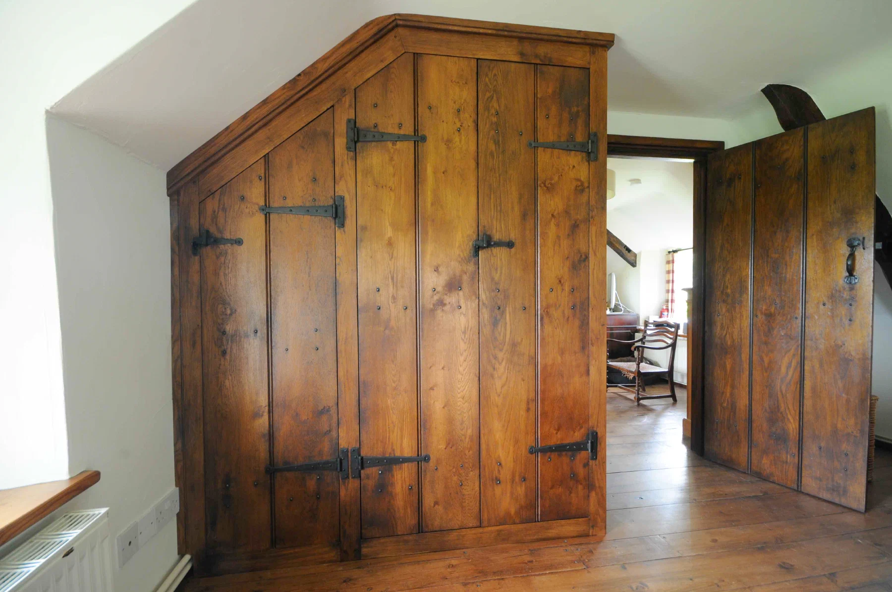 Eaves cupboard with ledged plank doors and strap hinges beneath a sloping ceiling