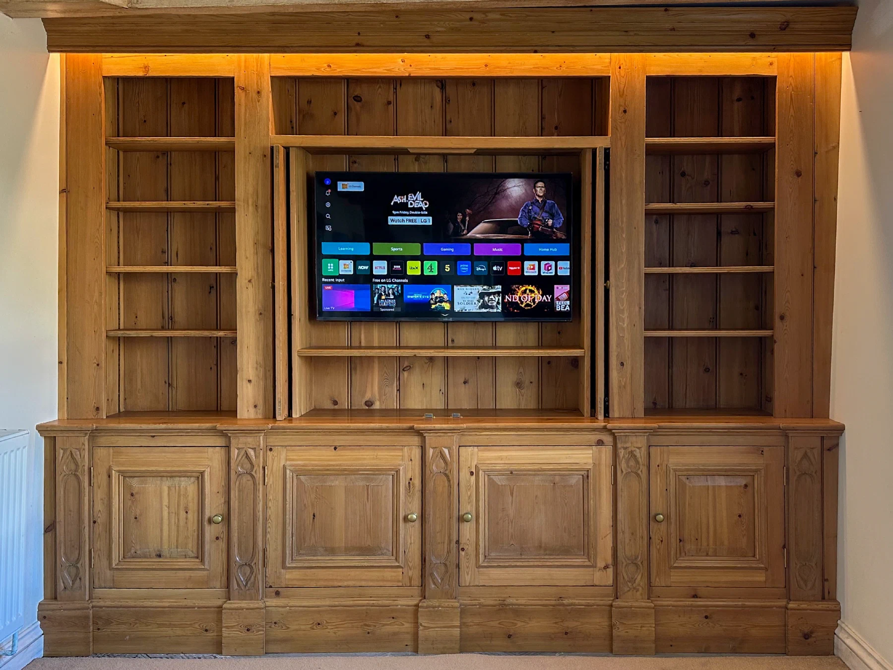 Fitted timber media cabinet with its central doors folded back to reveal the television