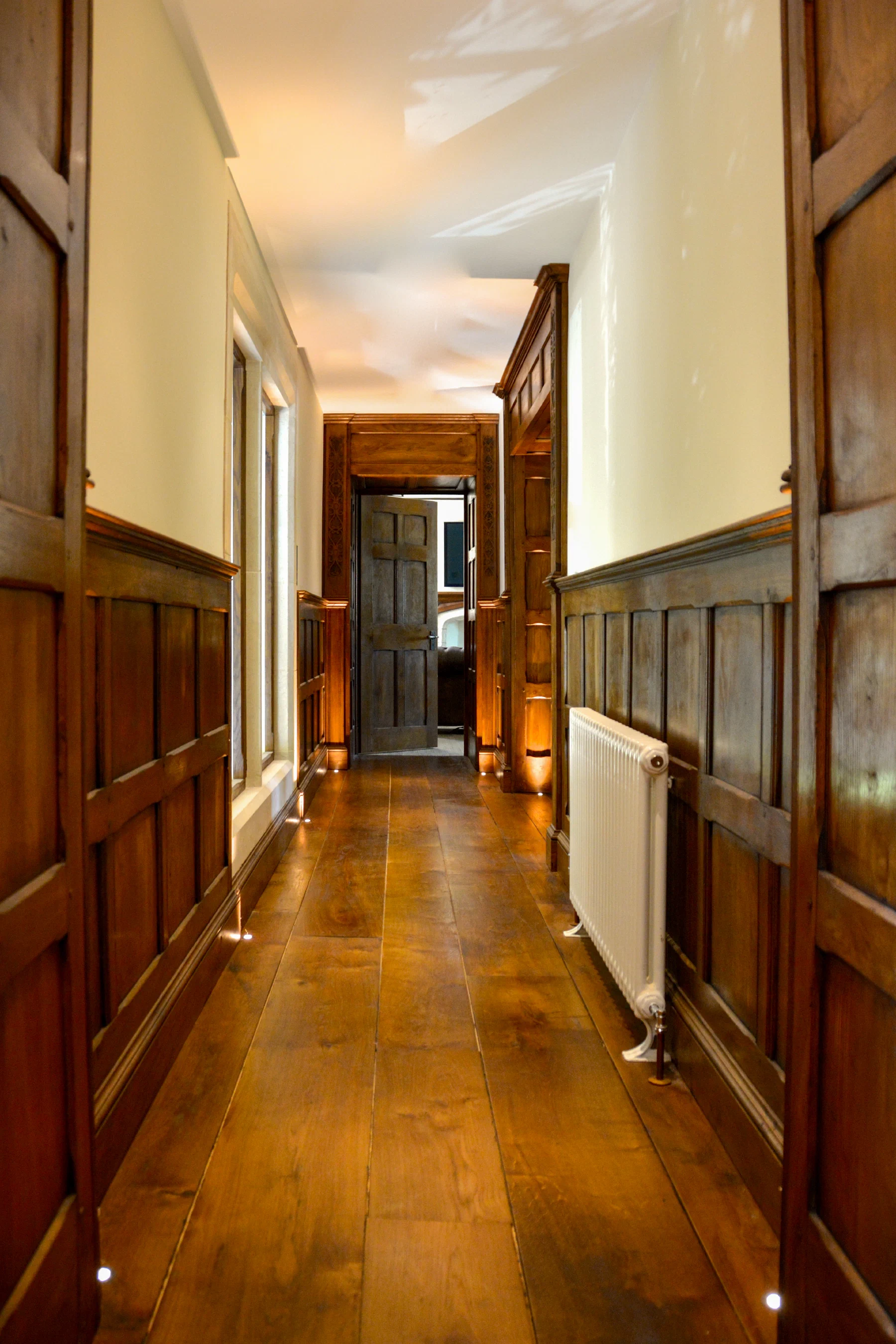 Oak-panelled corridor with wide-board floor and uplighting