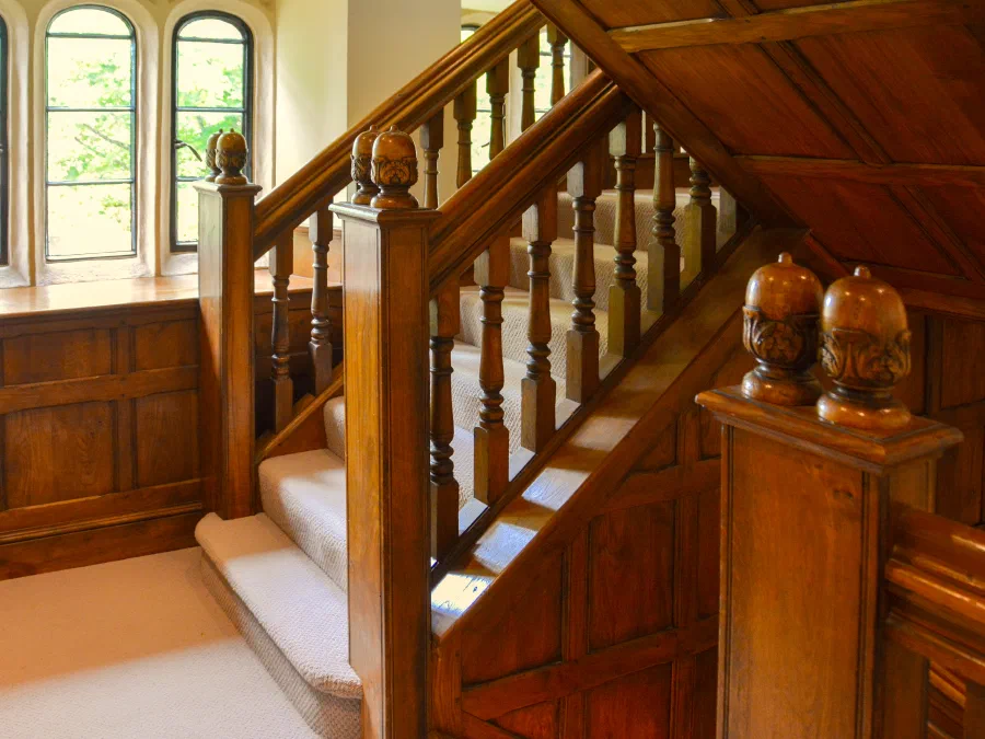 Oak staircase newel, balustrade and wall panelling beside a mullioned window