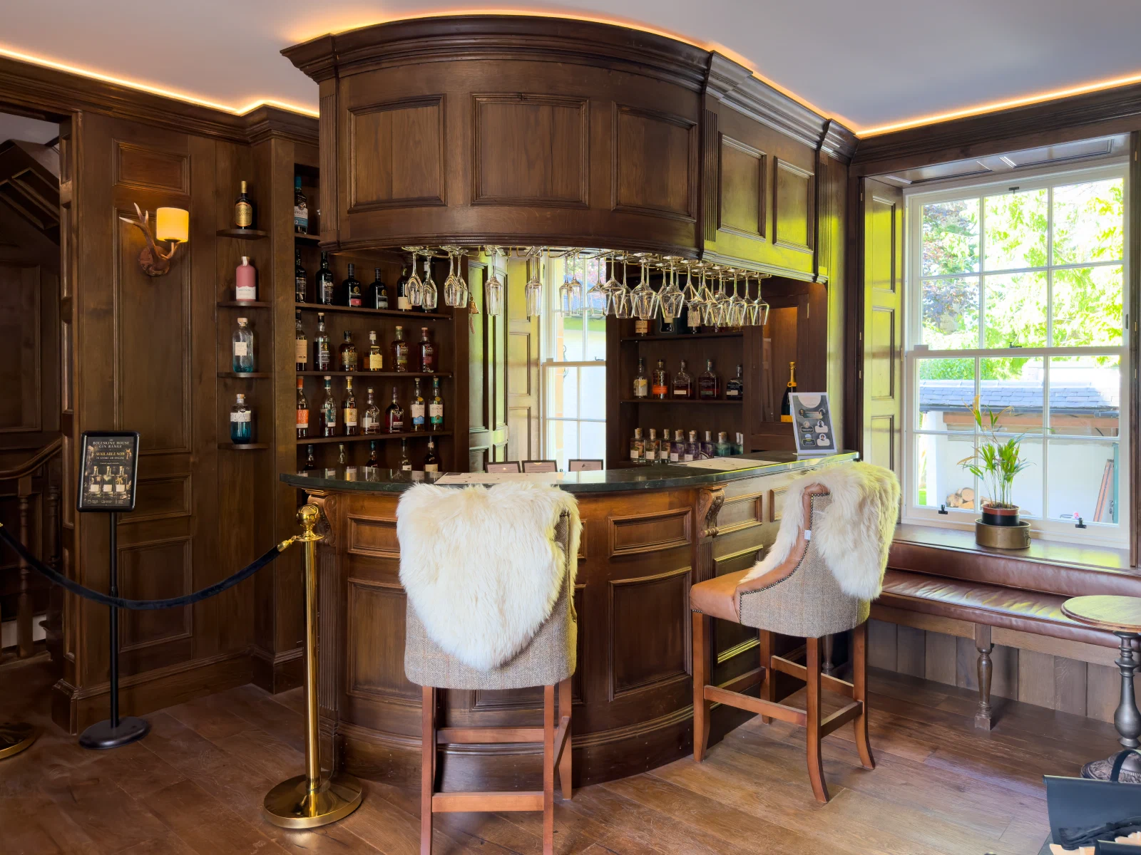 Curved oak whisky bar with an overhead canopy beside a sash window