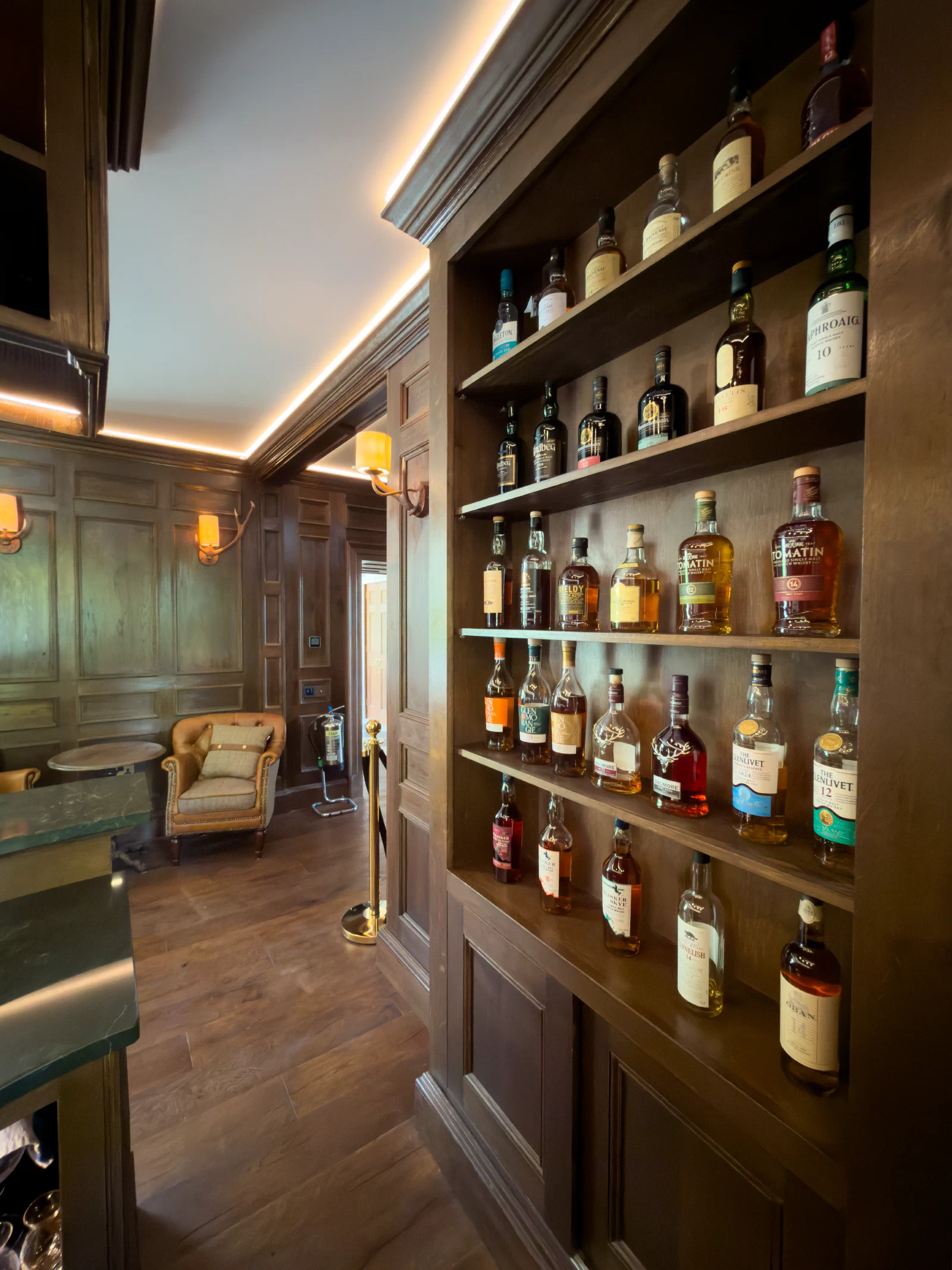 Tall illuminated whisky display shelving set into dark oak panelling
