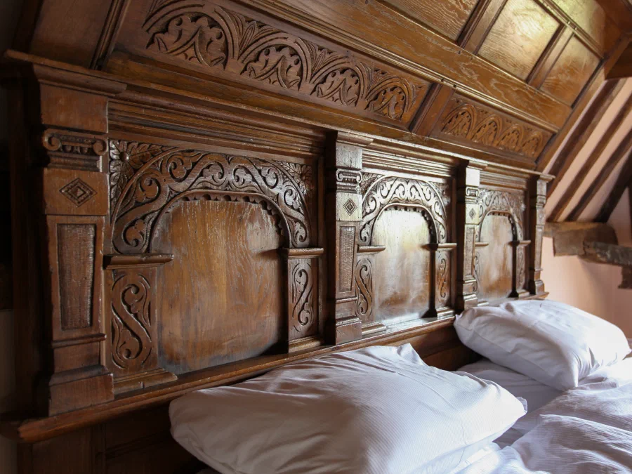 Carved oak headboard in a bedroom beneath sloping timber framing