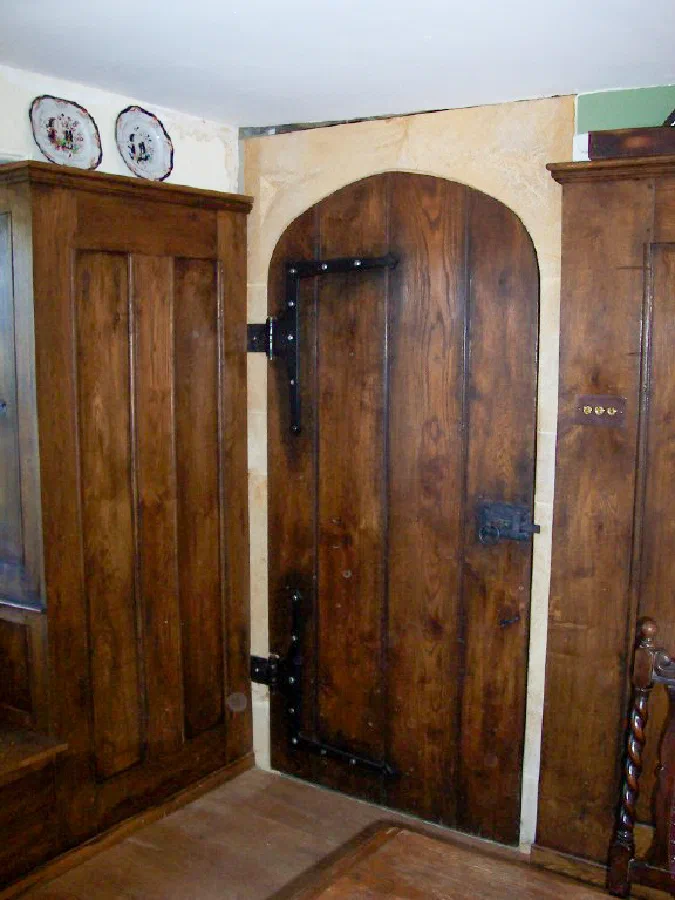 Arched plank door with dark strap hinges beside timber wall panelling