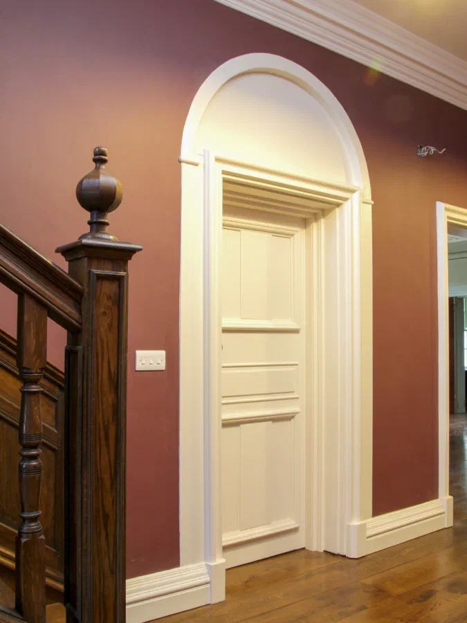 Painted panelled internal door with a classical architrave beside an oak staircase
