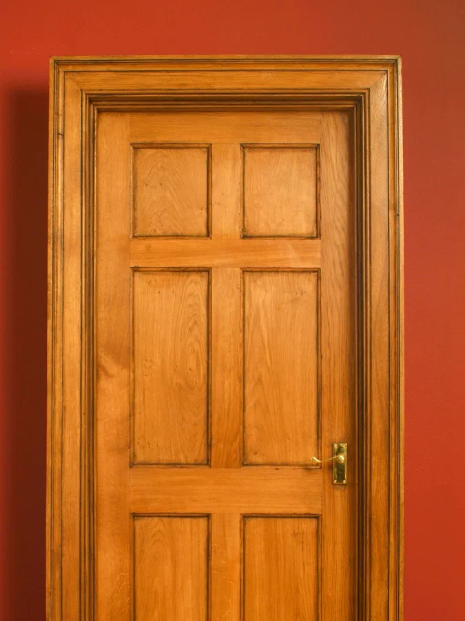 Six-panelled timber door with a moulded surround against a red wall
