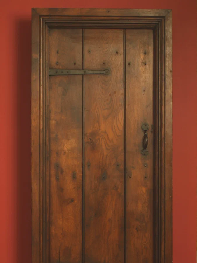 Internal oak plank door with traditional ironmongery and a moulded surround against a red wall