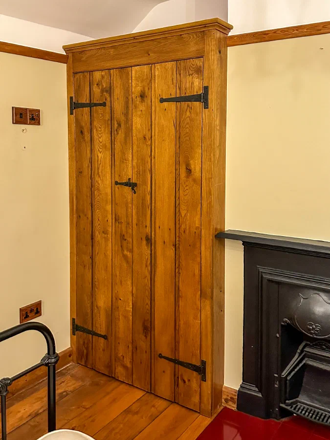Ledged internal oak plank door with strap hinges beside a cast-iron fireplace