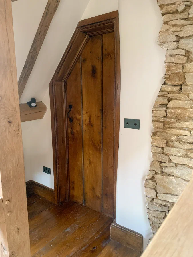 Internal oak plank door fitted to a sloping opening beside an exposed stone wall