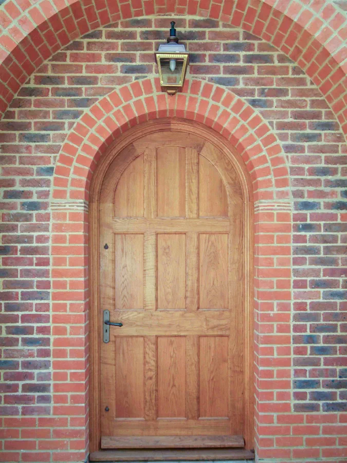 Arched oak door with raised and fielded panels in a red-brick arch