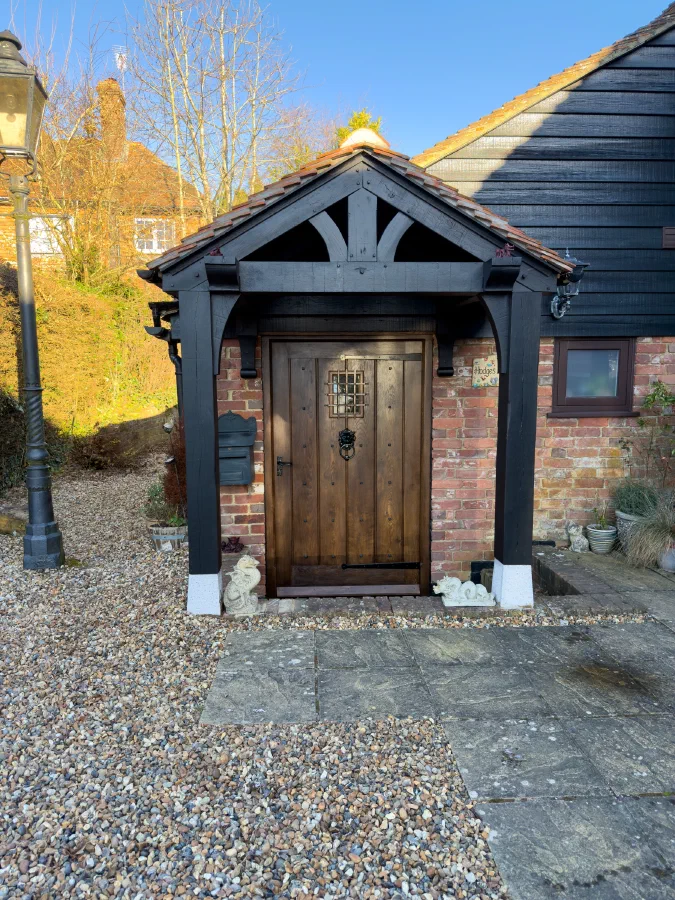 Dark-finished oak front door with a ring knocker beneath a black timber porch