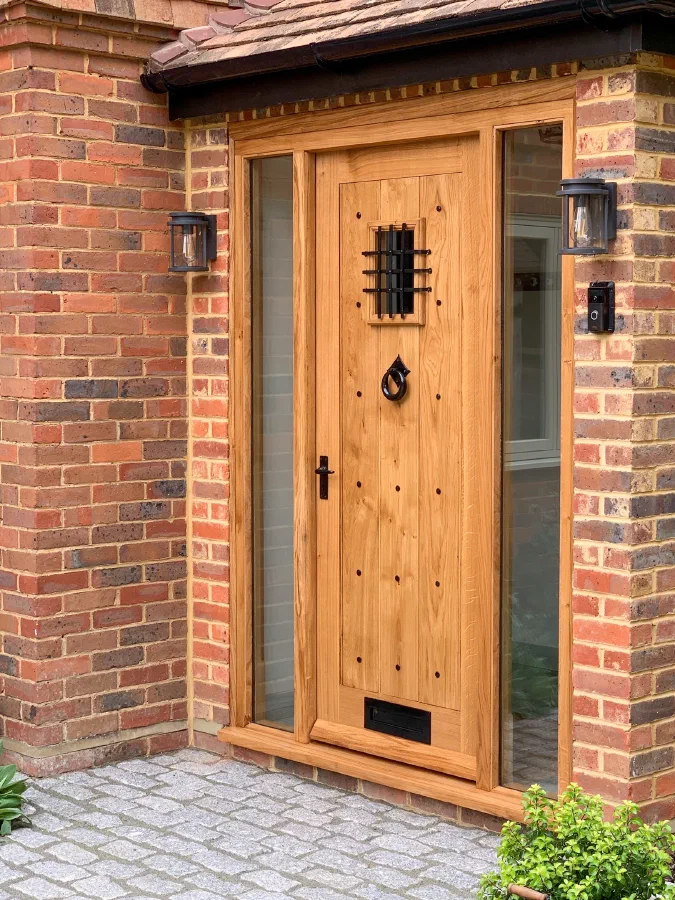 Oak plank door with an iron-grilled light, studwork and a full-height glazed sidelight in a brick porch