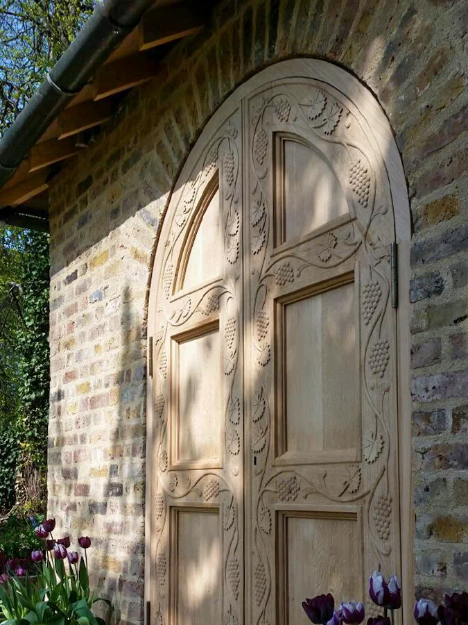 Arched oak door with carved vine decoration around its panels, set in a brick opening