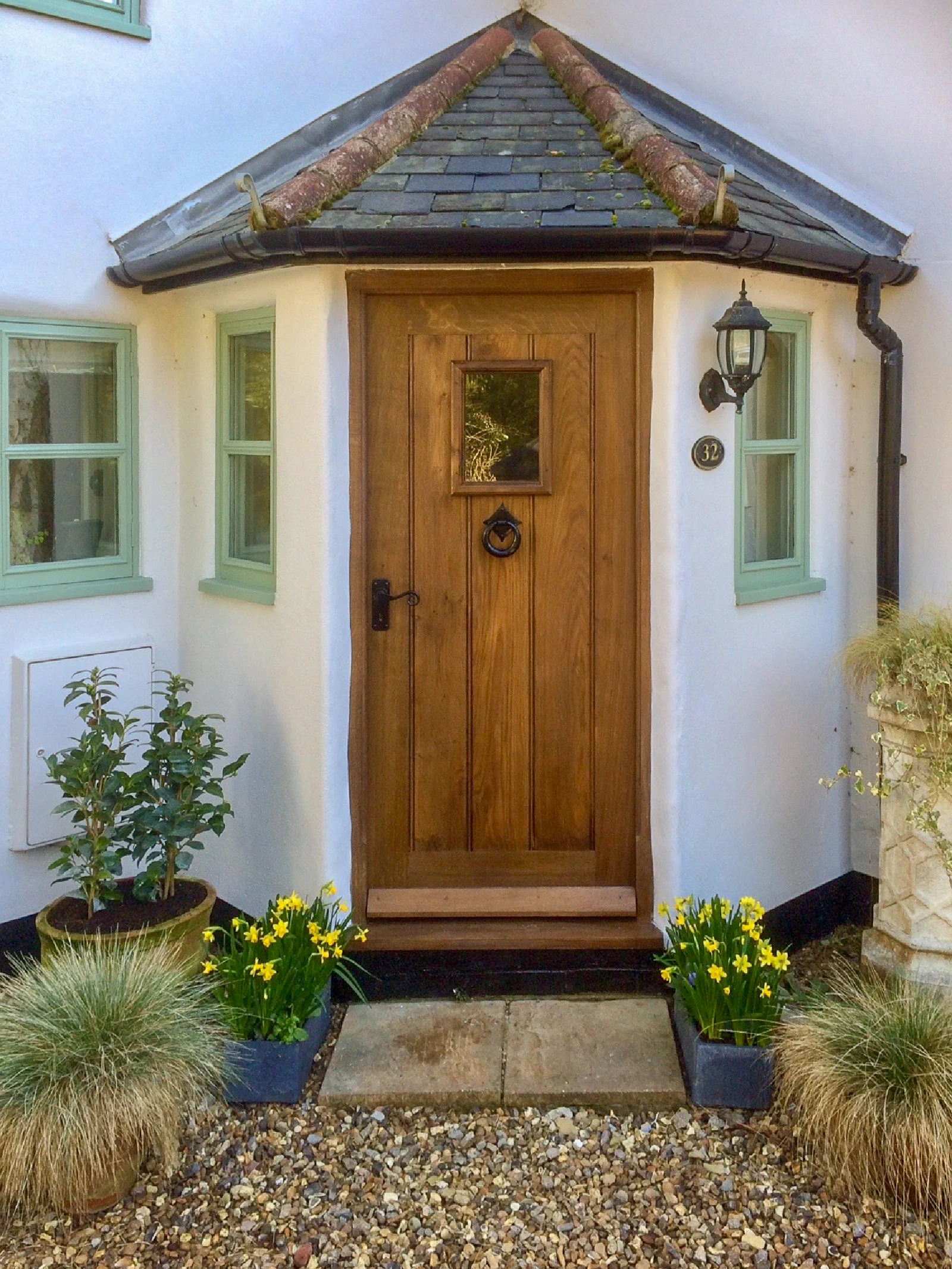 Oak framed plank front door with a small glazed light in a white rendered cottage porch