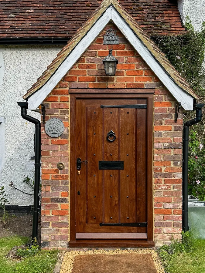 Studded boarded oak front door with a ring knocker and strap hinges in a brick porch