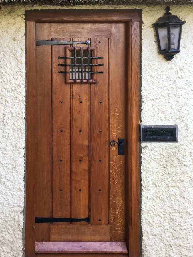 Studded oak plank door with an iron grille, strap hinges and a lever handle in a rendered wall