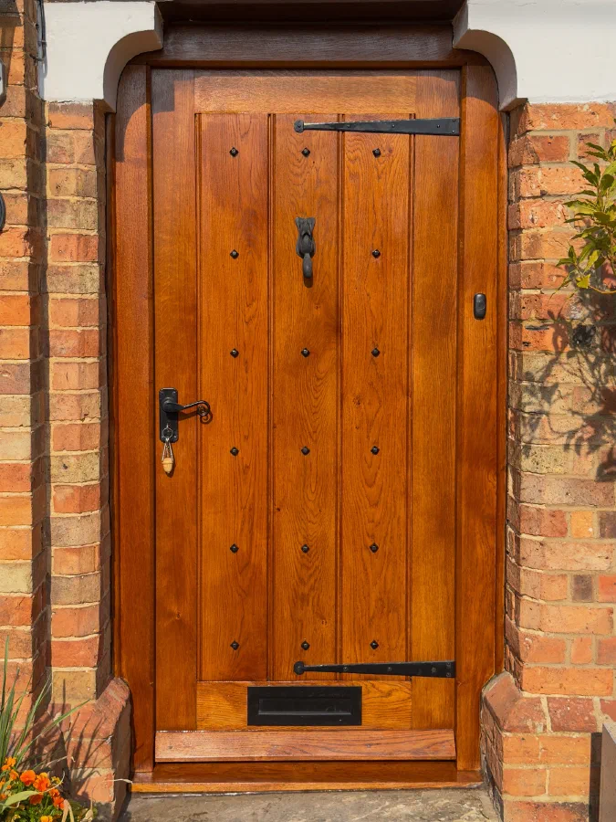 Studded oak door with strap hinges, a drop knocker and a letter plate under a shaped brick head