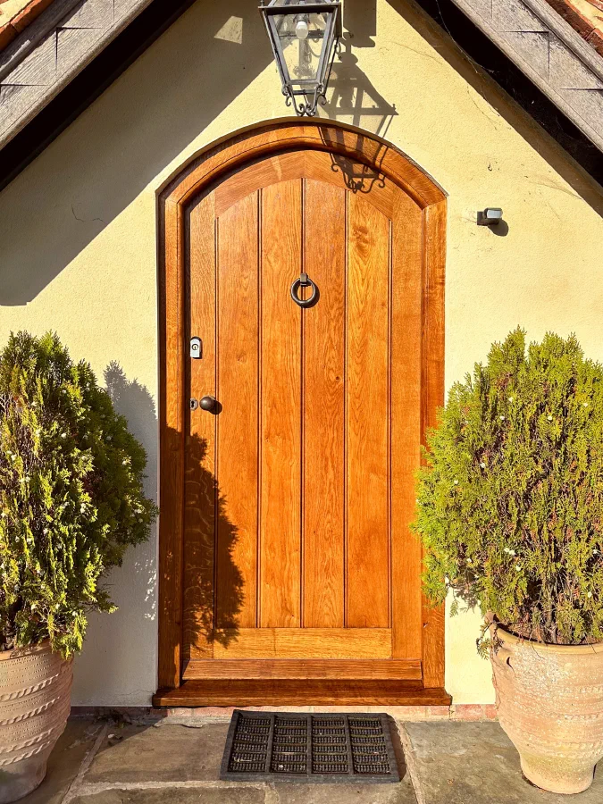 Arched oak framed plank door beneath a small entrance gable