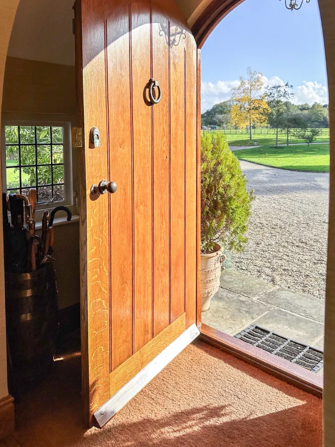 Arched oak plank door seen from inside the hall, open onto a gravel drive