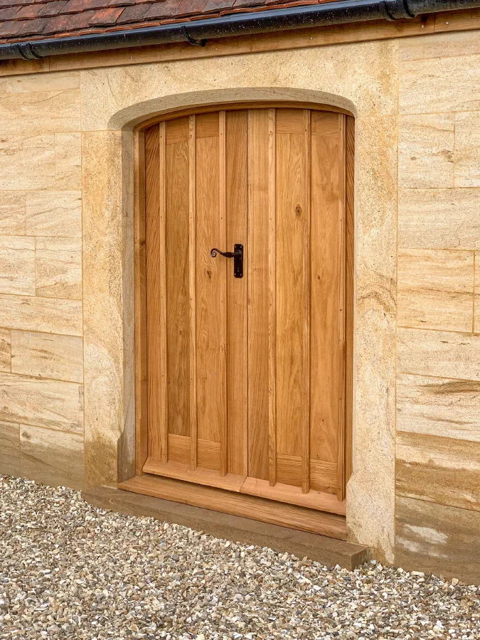 Arched oak plank door with a black latch handle in a sandstone wall