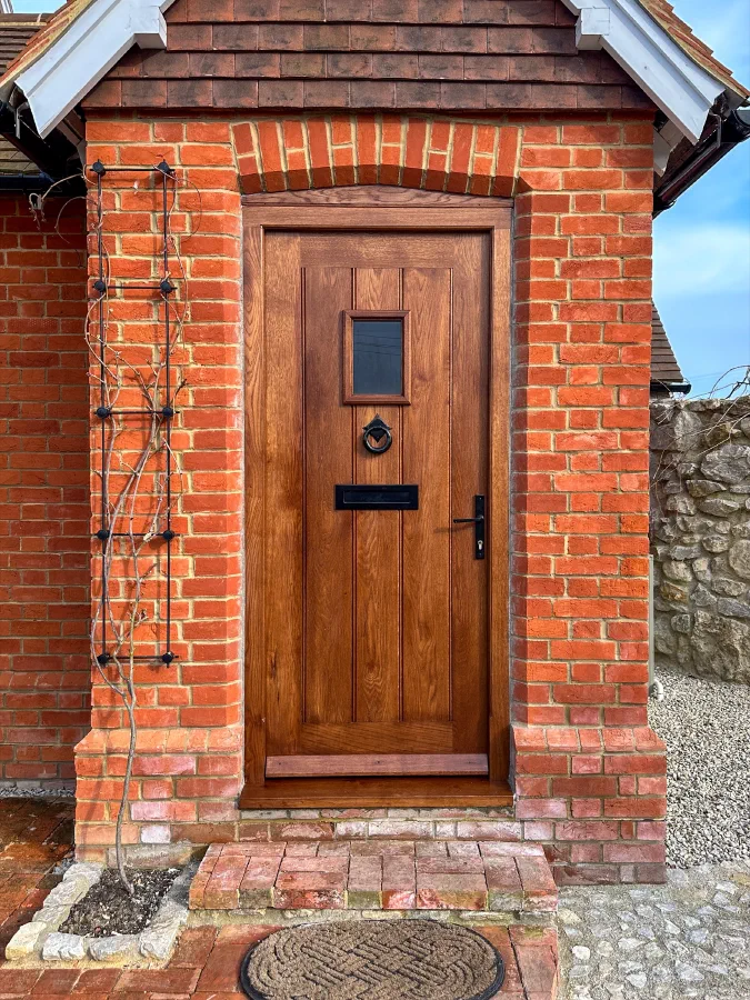 Framed plank oak door with a small glazed light, ring knocker and letter plate in a red-brick porch