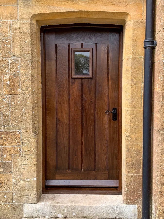 Dark oak framed plank door with a small glazed light in a dressed stone opening