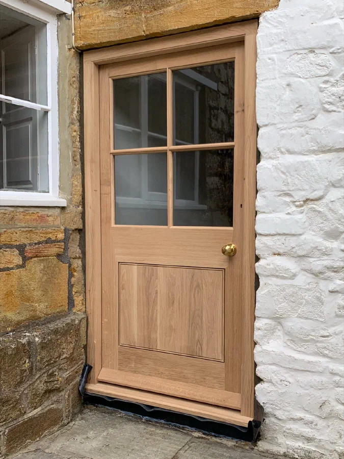 Half-glazed oak door with four lights above a single panel, set between stone and whitewashed walls