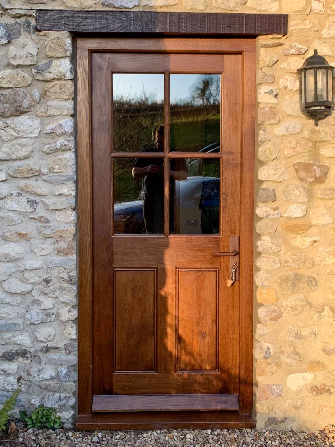Half-glazed oak front door with four lights above two panels, in a stone wall beneath an oak lintel