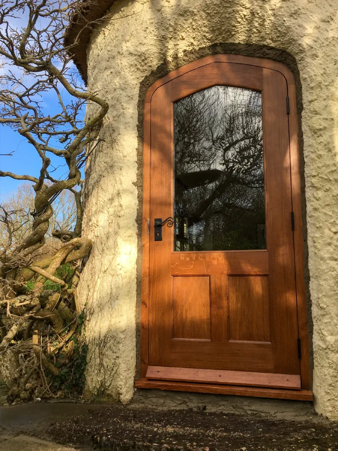 Arched half-glazed oak door with a single large light above two panels, in a rendered wall