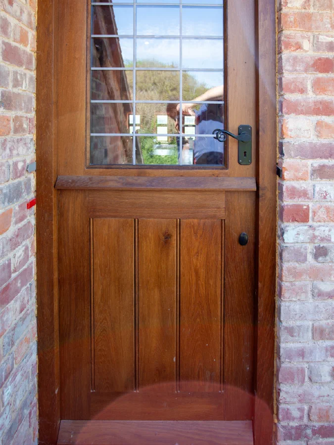 Half-glazed oak door with a leaded light above a boarded lower half, set in a brick opening