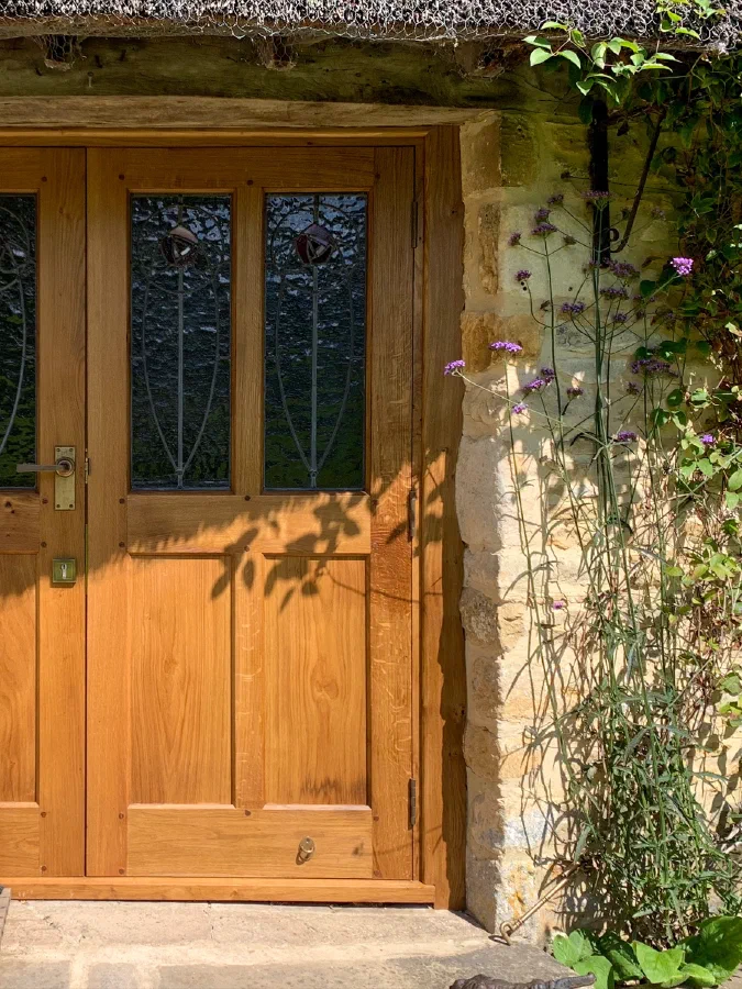 Pair of half-glazed oak doors with decorative leaded glass in a stone cottage entrance
