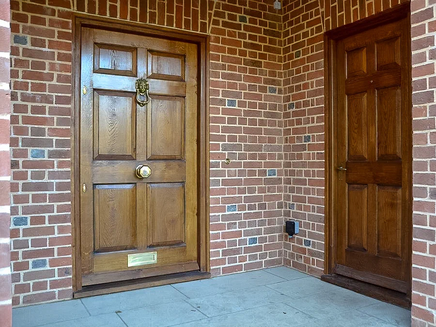 Six-panel oak front door in a brick porch, with a second panelled door at the side