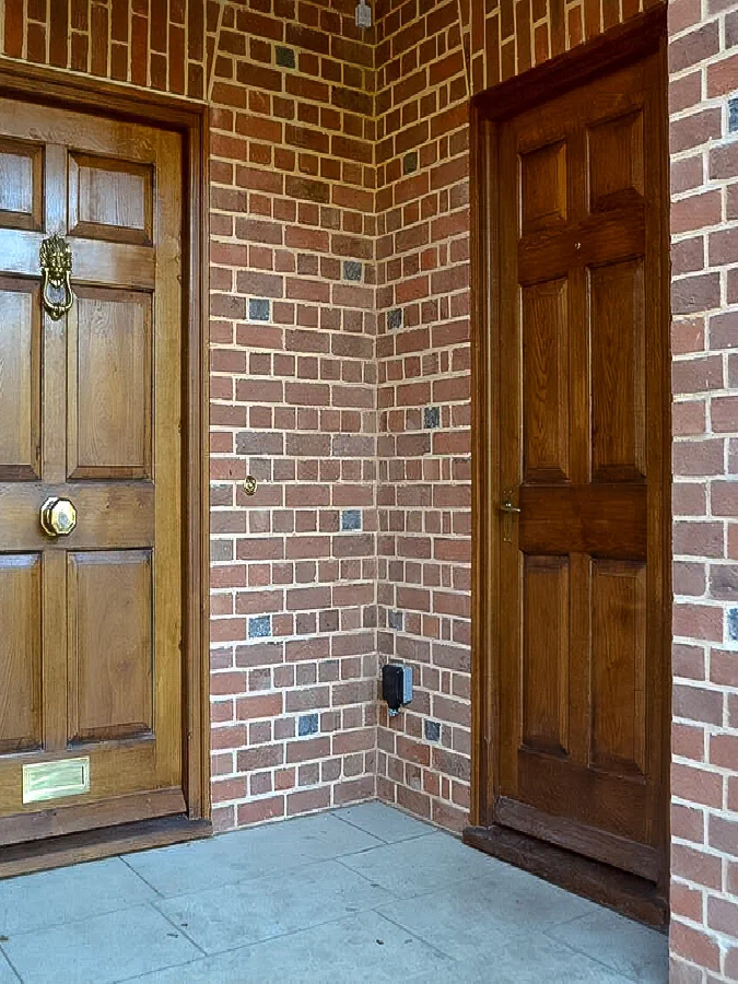 Six-panel oak front door in a brick porch, with a second panelled door at the side