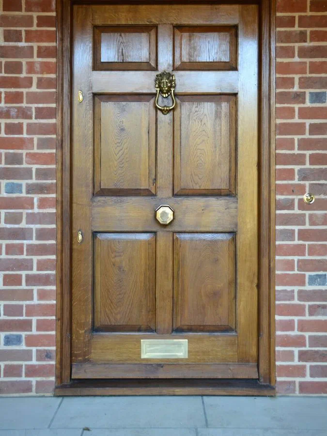 Six-panel oak front door with raised and fielded panels, a lion-head knocker, centre knob and letter plate, in a brick opening
