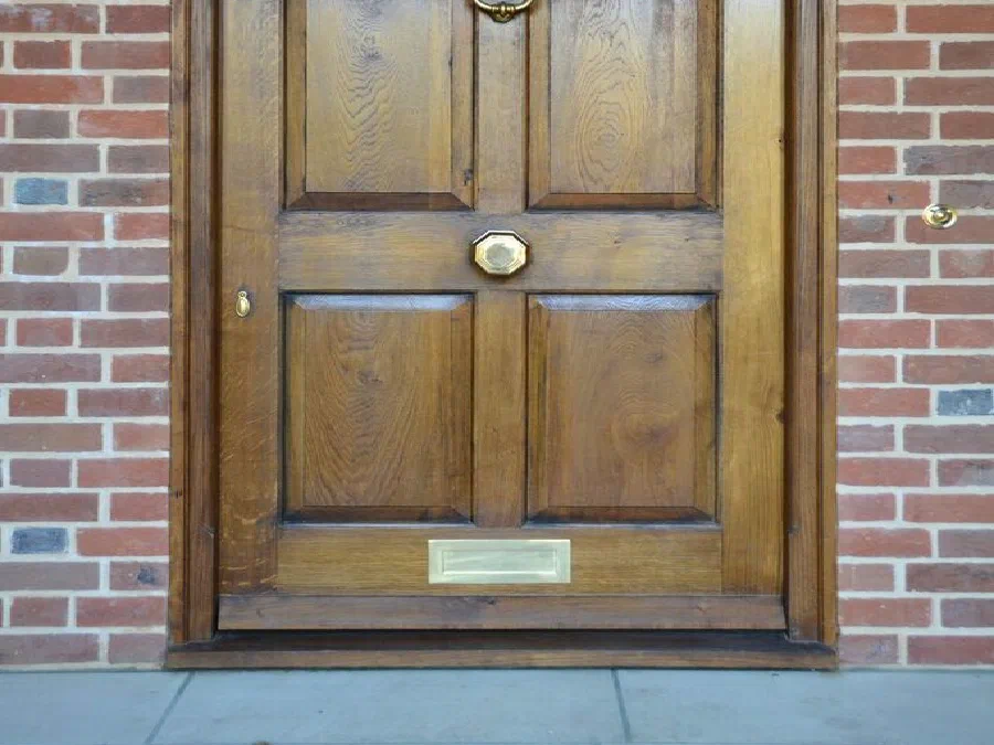 Six-panel oak front door with raised and fielded panels, a lion-head knocker, centre knob and letter plate, in a brick opening