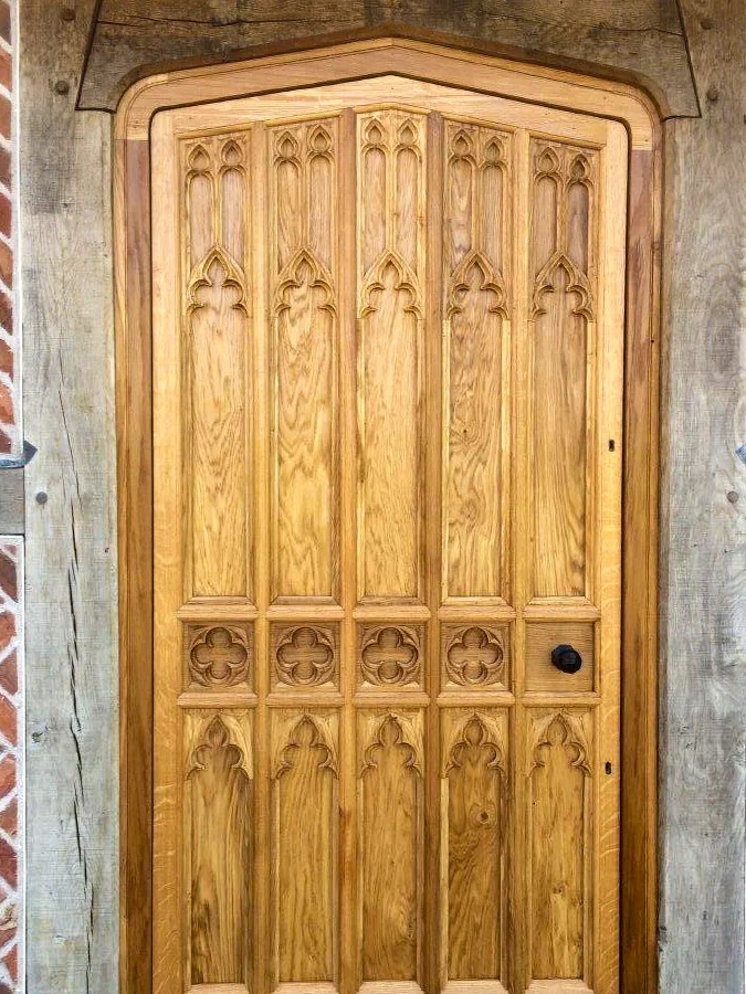 Oak door with carved Gothic tracery panels under an arched head, set in a timber-framed opening