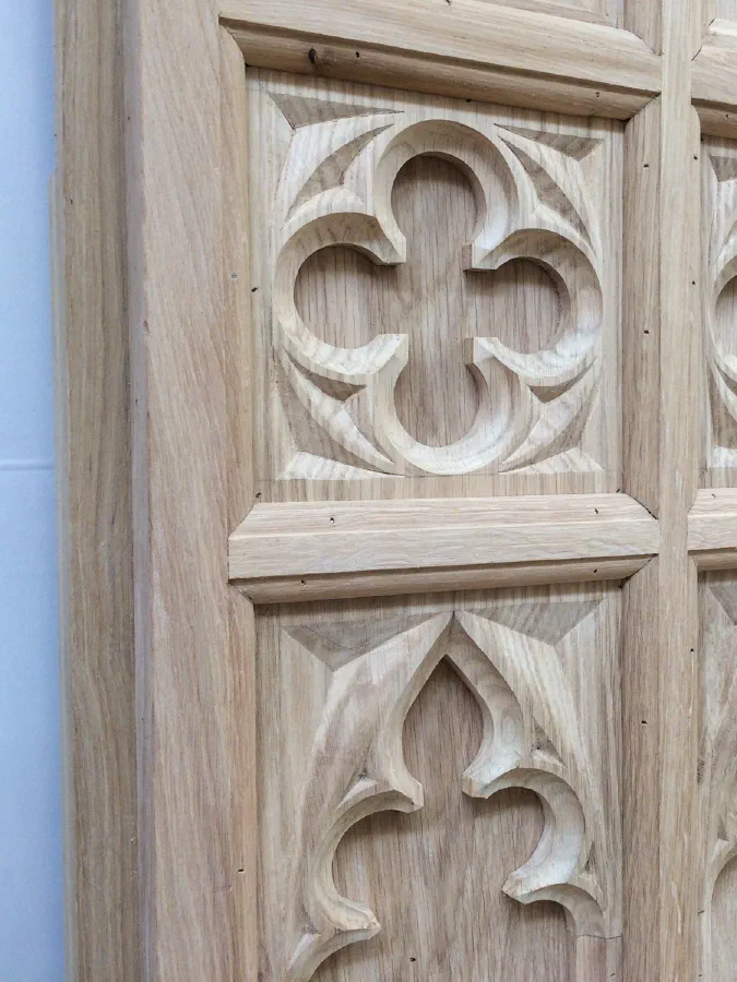 Close view of carved quatrefoils above cusped tracery panels in oak