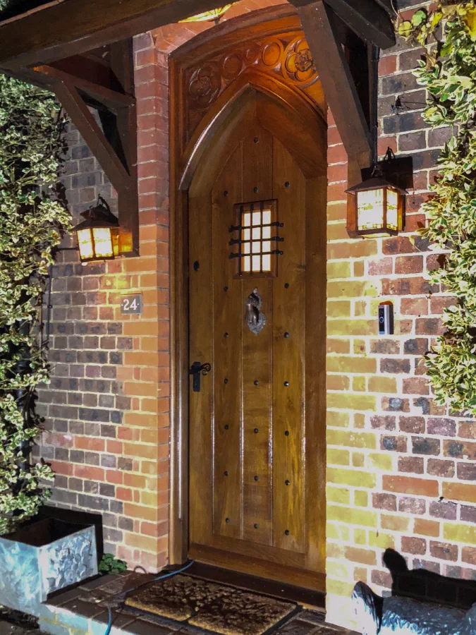 Oak door with a pointed Gothic head, an iron-grilled light and studwork beneath a carved timber porch