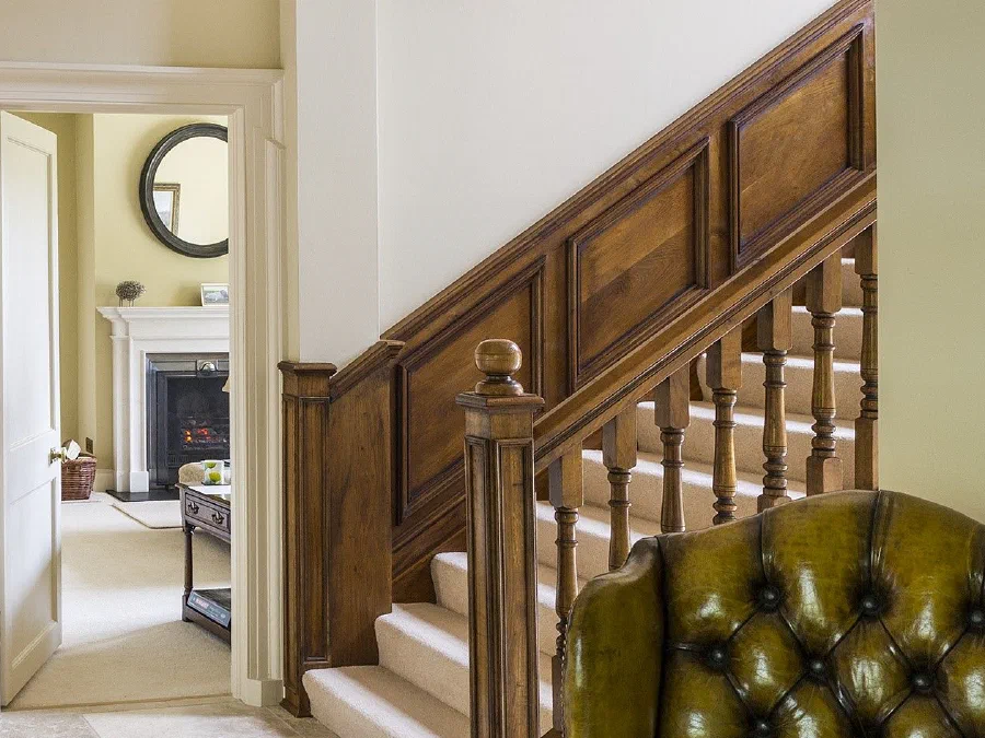 Oak staircase with panelled dado and turned balusters rising from a stone-floored hall