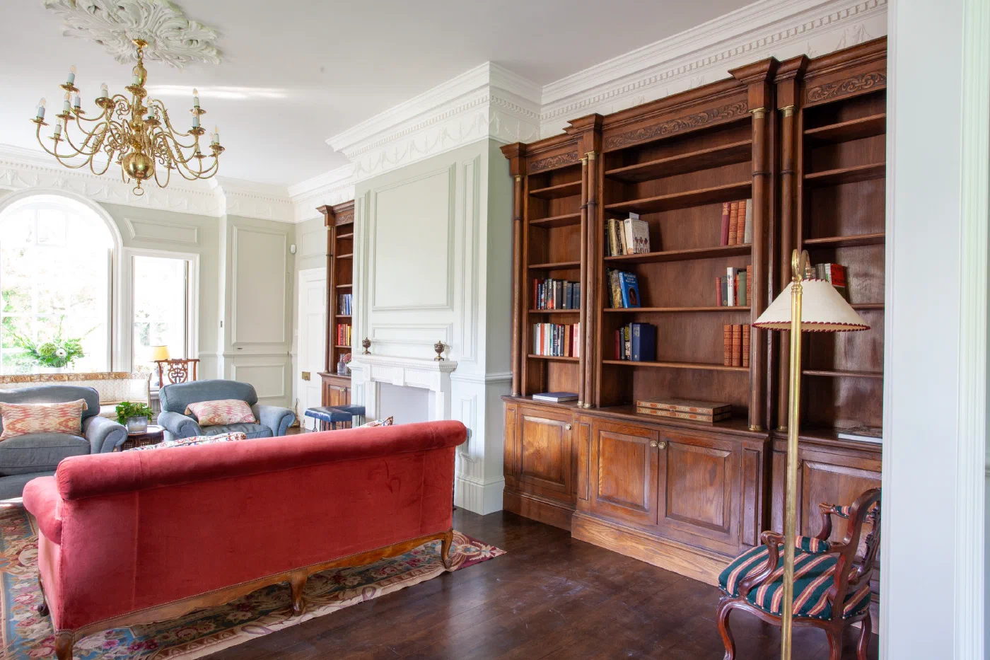 Painted wall panelling around a fireplace with oak bookcases alongside at Alderwick House