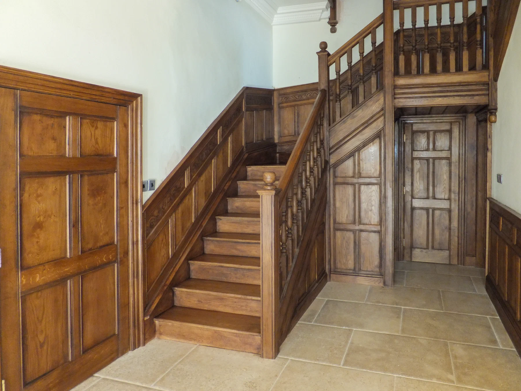 Closed-string oak staircase integrated with wall panelling and panelled doors