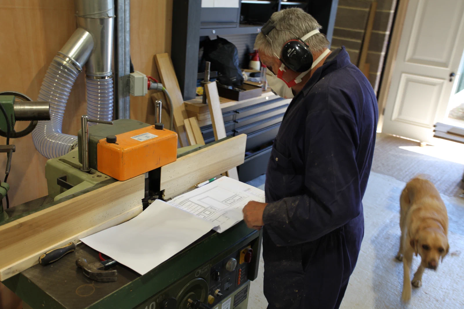 Craftsperson reviewing a joinery drawing beside a workshop machine