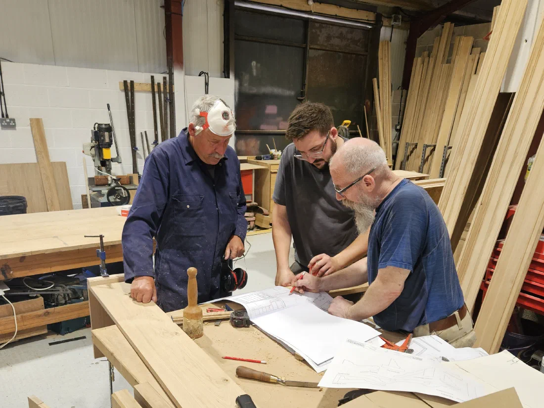 Three of the team going through drawings at a workbench in the Somerset workshop